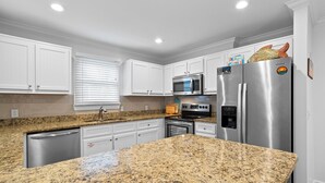 Una cocina moderna con armarios blancos, encimeras de granito y electrodomésticos de acero inoxidable, incluyendo un horno empotrado.
