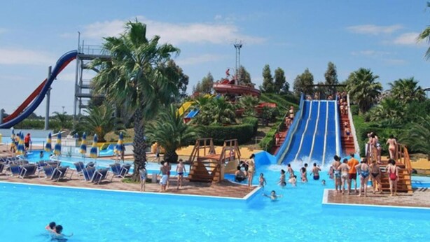 Un parque acuático con una piscina grande, varias toboganes y palmeras.