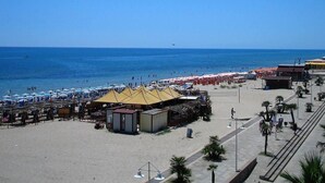 Una playa con numerosos paraguas y carpas, una zona arenosa y un cielo azul despejado.
