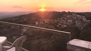 Vista del atardecer desde un balcón con vistas a un pueblo y aerogeneradores a lo lejos.
