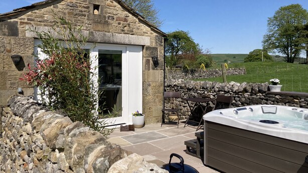 Une charmante maison en pierre dotée d’un jacuzzi, d’un espace extérieur aménagé et d’un mur en pierre.