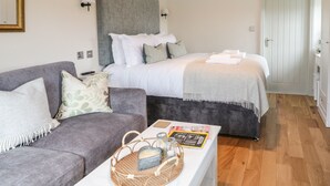 Une chambre à coucher moderne avec un canapé gris, un lit blanc doté d’une tête de lit grise et un plancher en bois.