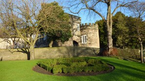 Un bâtiment historique en pierre, doté d’une tourelle et de créneaux, entouré de pelouses bien entretenues et d’arbres majestueux.