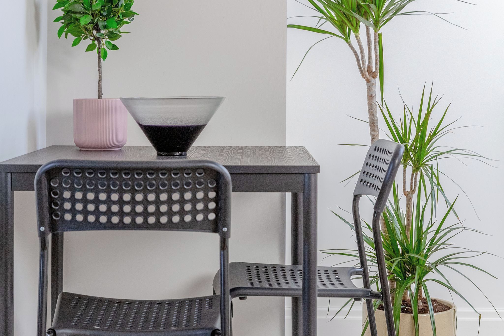 A modern chair with a perforated backrest and a table with a pink vase and a black bowl.
