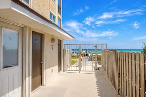 A corridor leading to a beach with a wooden fence on one side and a building entrance on the other.
