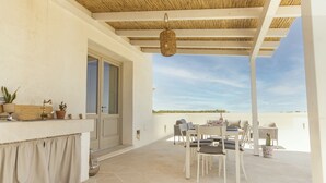 A covered outdoor patio with a dining set, a hanging light fixture, and a view of the landscape. - Masseria Macchiaforte (Gallipoli)