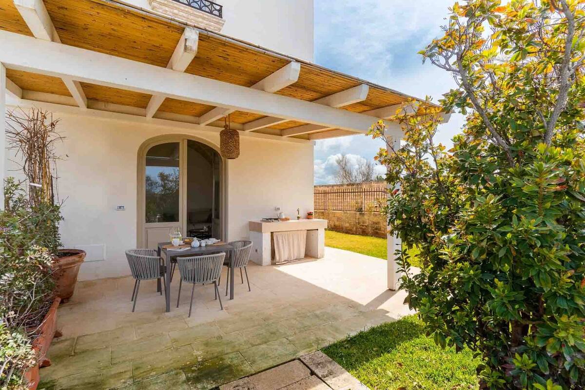 A patio with a dining table and chairs, a small kitchen area, and a garden with a wooden fence.