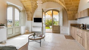 A spacious living area with a high arched ceiling, a round glass coffee table, and a television mounted on the wall. - Masseria Macchiaforte (Gallipoli)