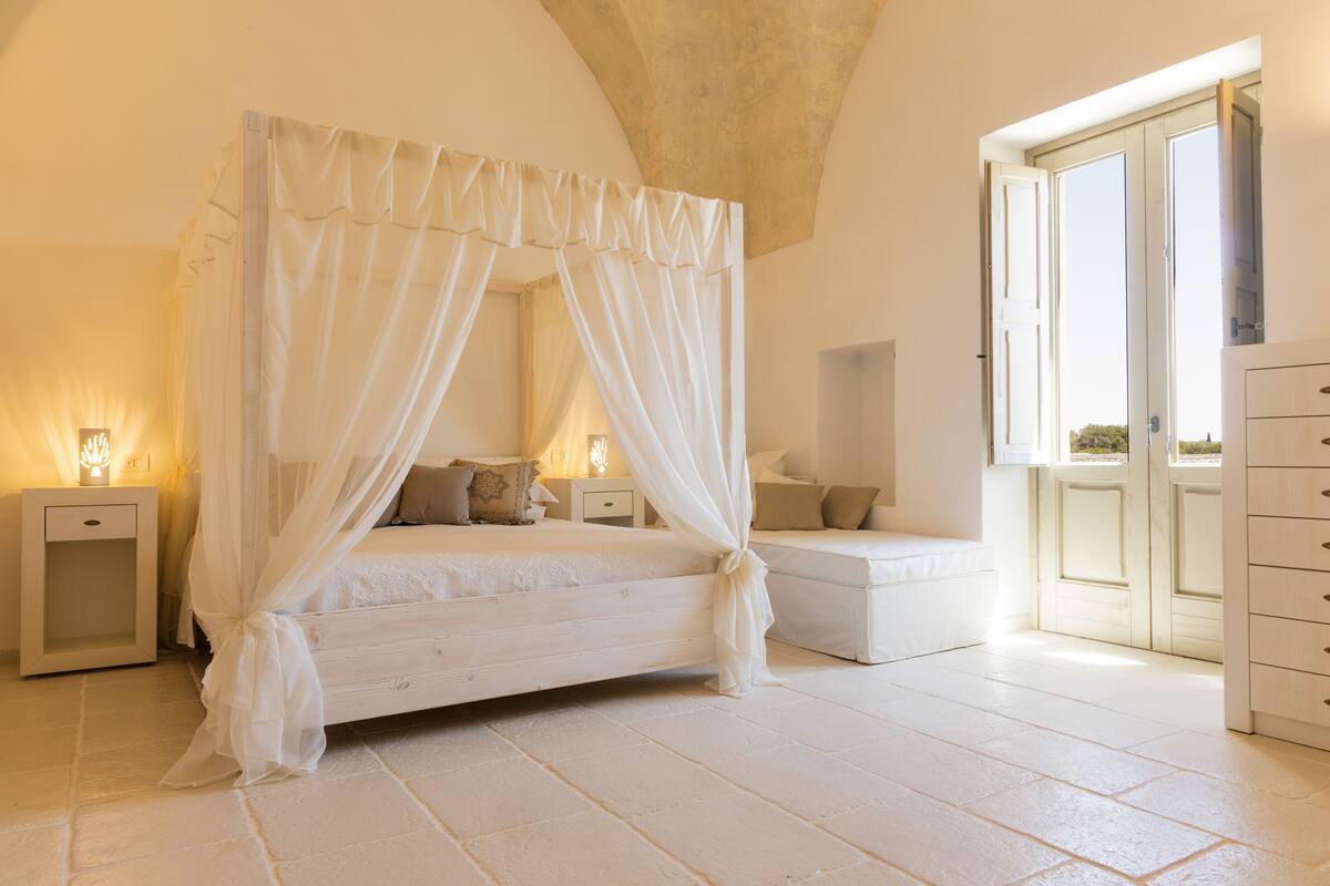 A bedroom with a four-poster bed, bedside tables, a nightstand, and a dresser.