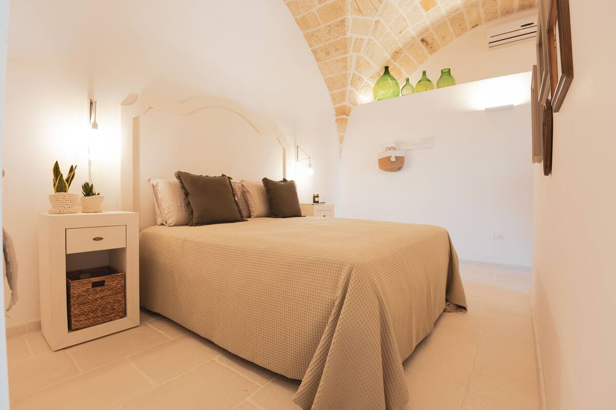 A bedroom with a bed, bedside tables, a lamp, and a wall-mounted shelf with bottles.