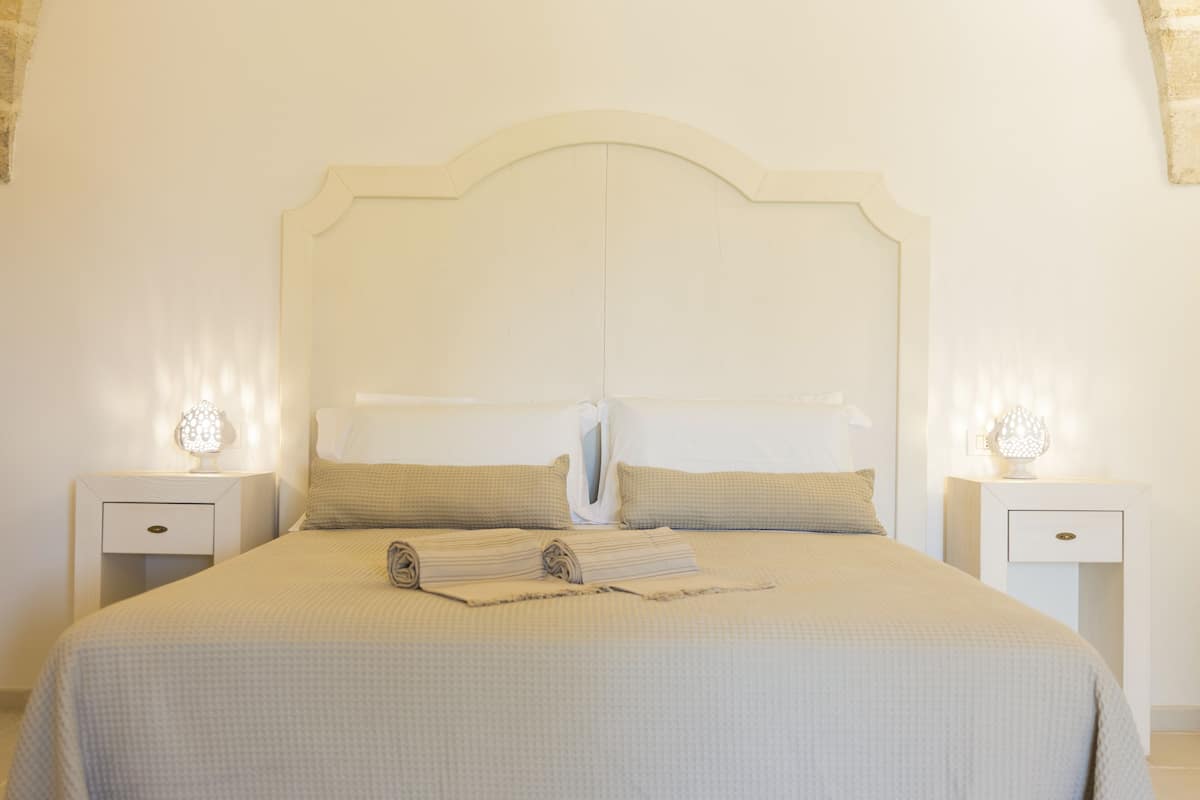 A neatly made bed with a headboard, two bedside tables with lamps, and a folded towel on the bed.