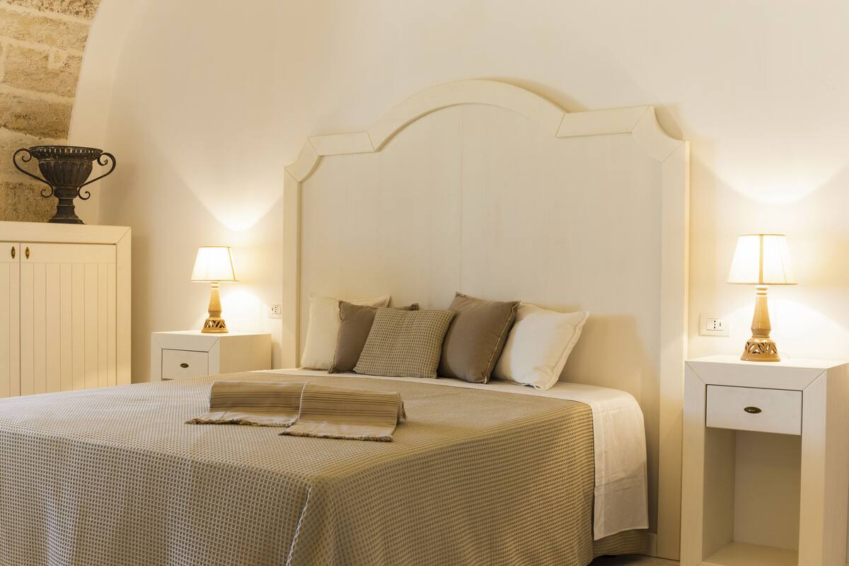 A neatly arranged bedroom with a bed, two bedside tables with lamps, a nightstand, and a decorative item on the left.