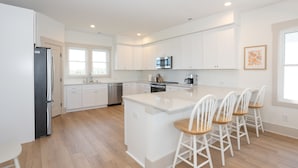 A modern kitchen with white cabinetry, a central island with bar stools, a stainless steel refrigerator, and a dishwasher. - Lakefront Oasis w/ panoramic views on private road (Carolina Beach)