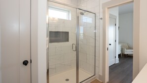 A modern bathroom with a glass shower enclosure, white marble tiles, and a wooden floor. - Lakefront Oasis w/ panoramic views on private road (Carolina Beach)