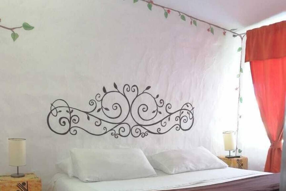 Habitación individual con una cabecera decorativa, una mesita de noche con lámpara y una cortina roja.