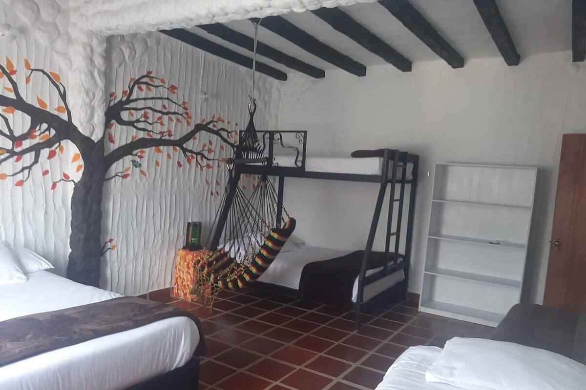 Una habitación con literas, una hamaca, un mural de un árbol y suelo de baldosas.