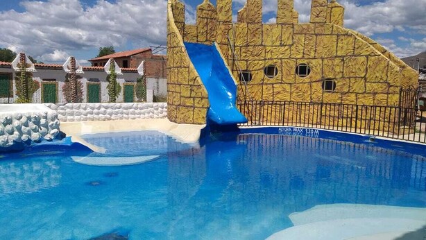 A swimming pool with a castle-like slide structure, surrounded by a fence and a stone wall. - VILLA LUISA HOTELS (Sáchica)