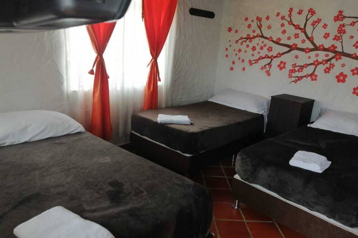 Habitación de hotel con dos camas, una cortina roja y un mural en la pared de un árbol con flores rojas.