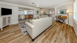 A spacious living room with a white sofa, wooden flooring, a flat-screen TV, and a dining area with a table and chairs. - The Lemon Bay Getaway (Venice)