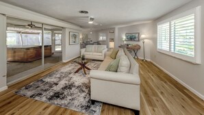 A spacious living room with a large glass sliding door leading to a patio, a white sofa, a coffee table, and a wooden floor. - The Lemon Bay Getaway (Venice)