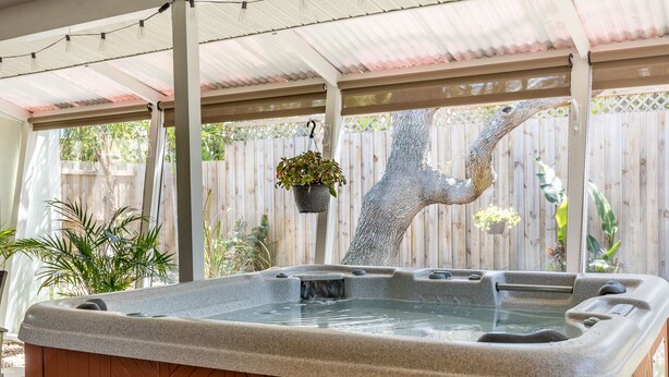 A hot tub under a covered patio with a wooden fence and hanging plants. - The Lemon Bay Getaway (Venice)