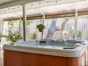 Un bain à remous installé sous une terrasse couverte, agrémentée d’une clôture en bois et de plantes suspendues.