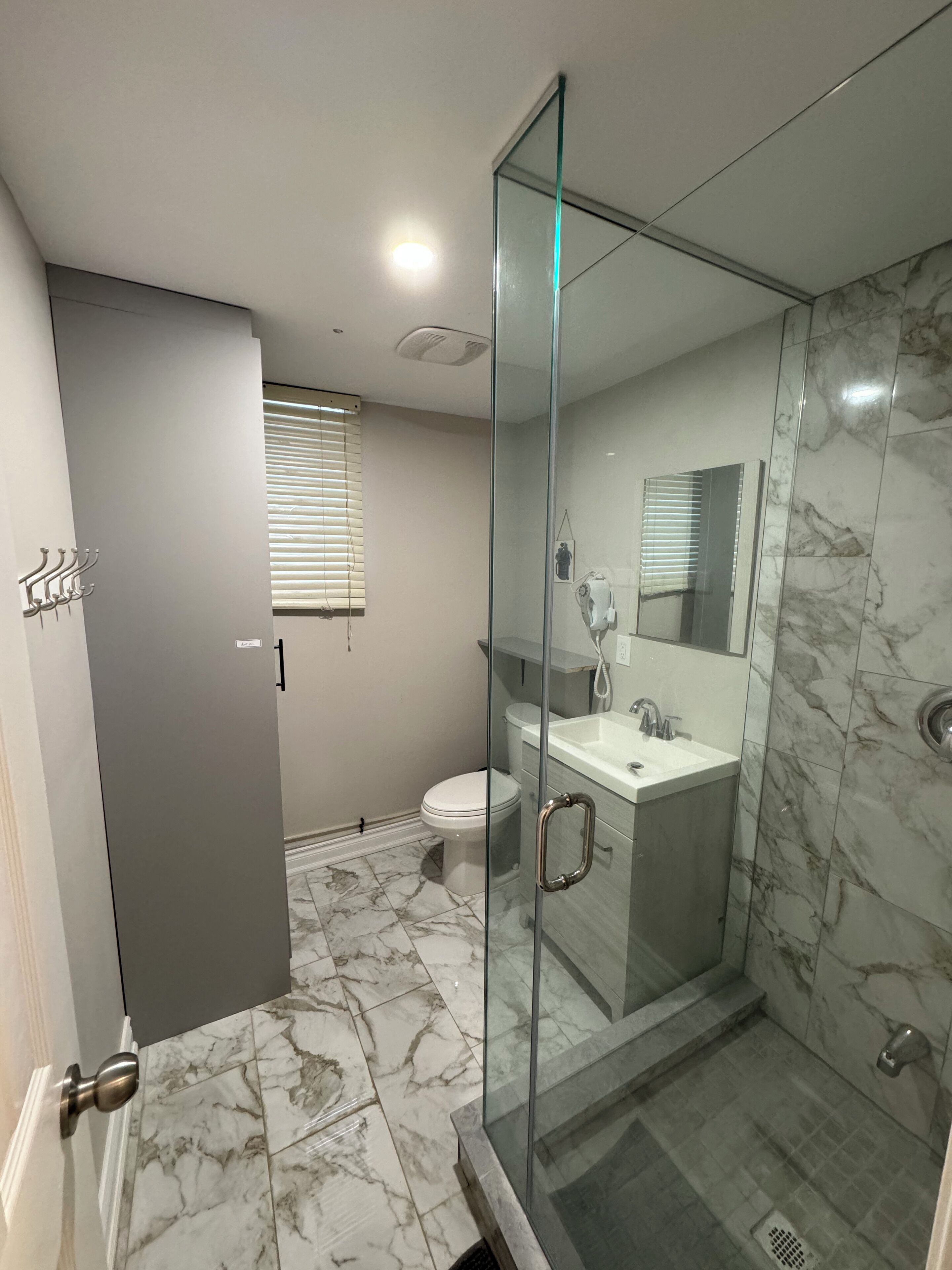 Un baño moderno con ducha de vidrio, inodoro y lavabo con encimera de mármol.