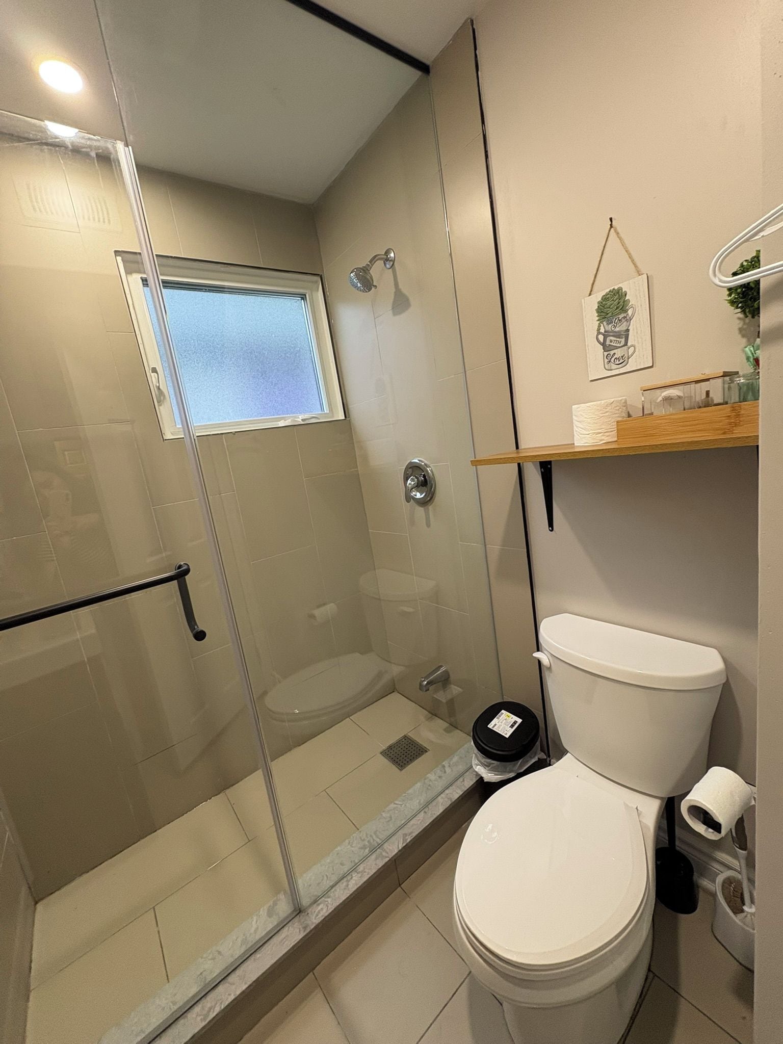 Un baño moderno con ducha de vidrio, inodoro y ventana pequeña.