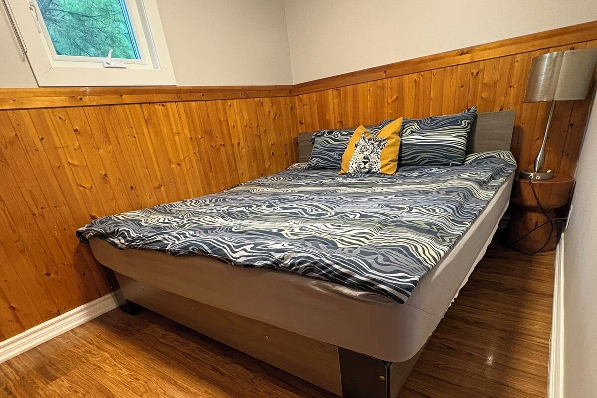 A bedroom with a bed, wooden flooring, a window, and a lamp.