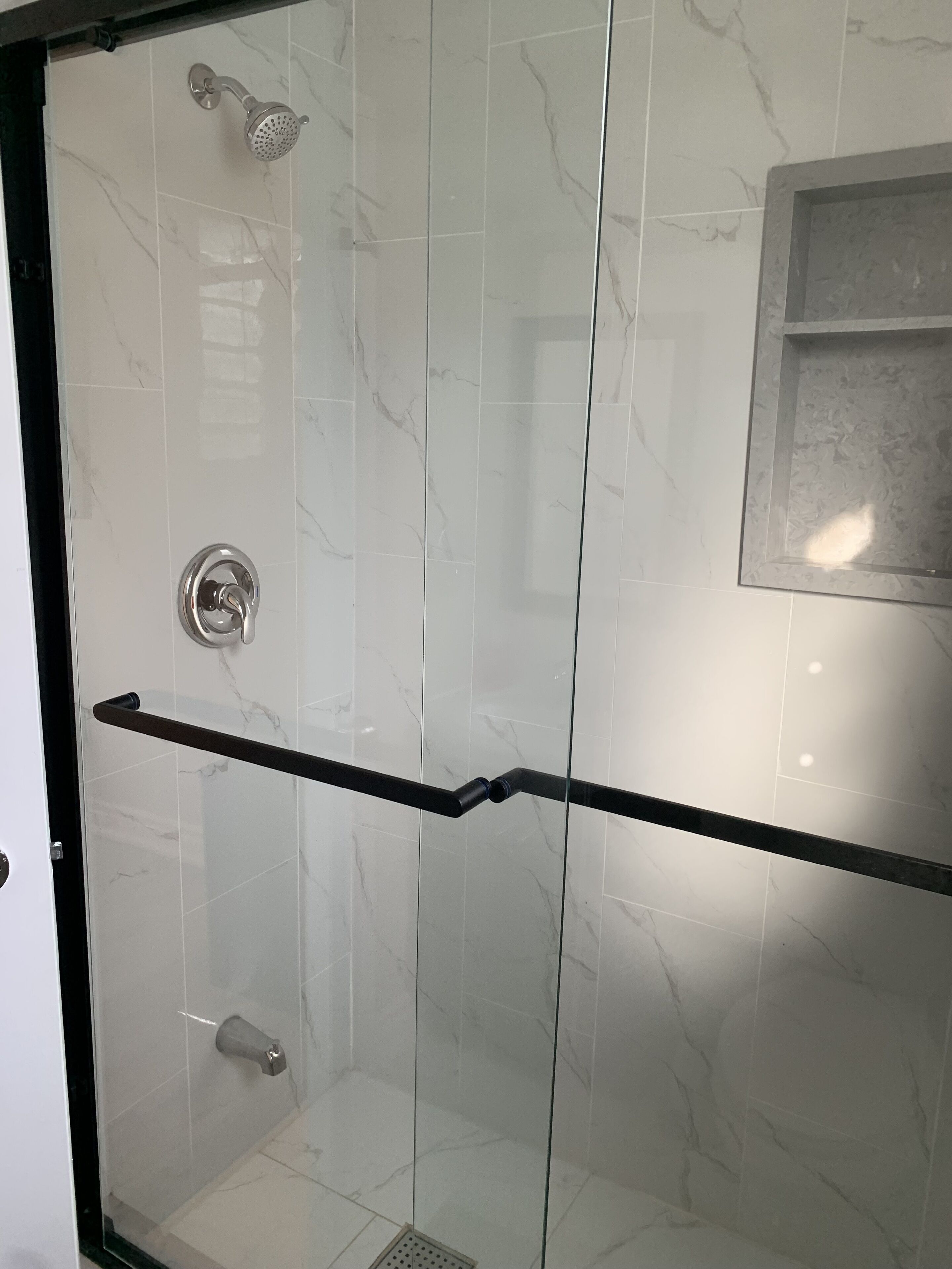 A glass-enclosed shower with a handheld showerhead and a handheld shower attachment.