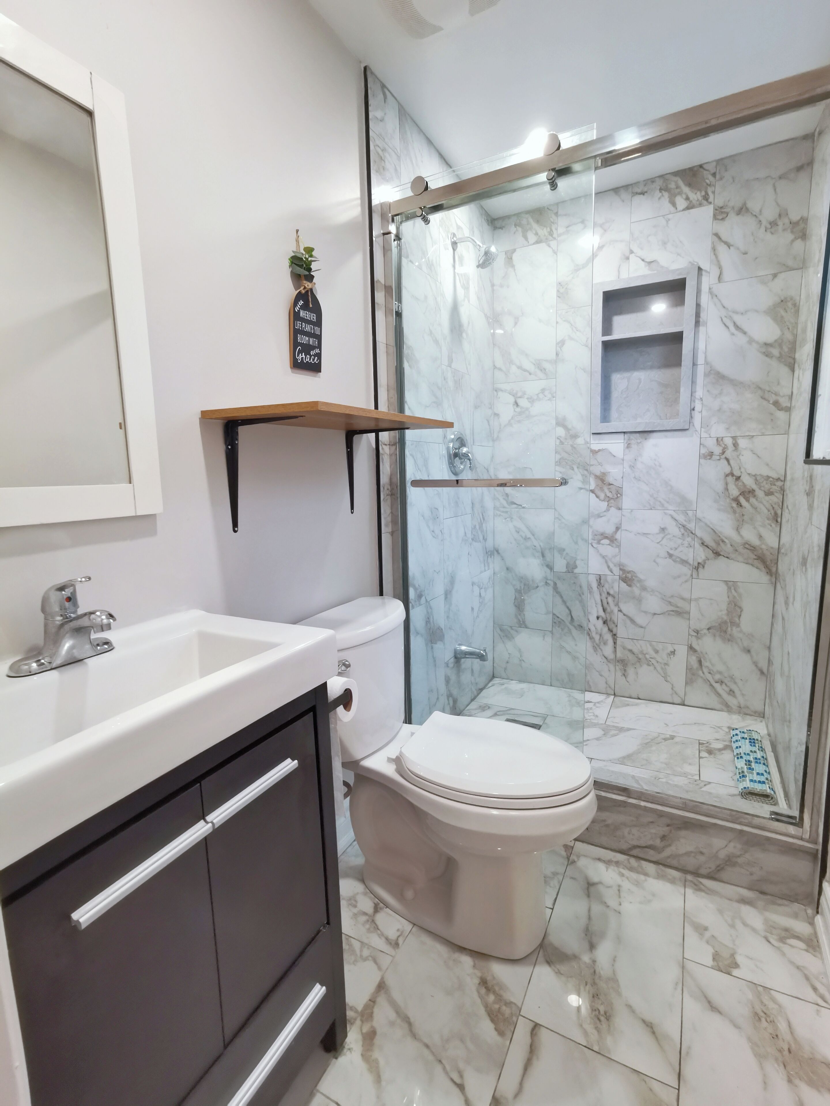 A bathroom with a white sink, a toilet, and a glass-enclosed shower area with marble tiles.