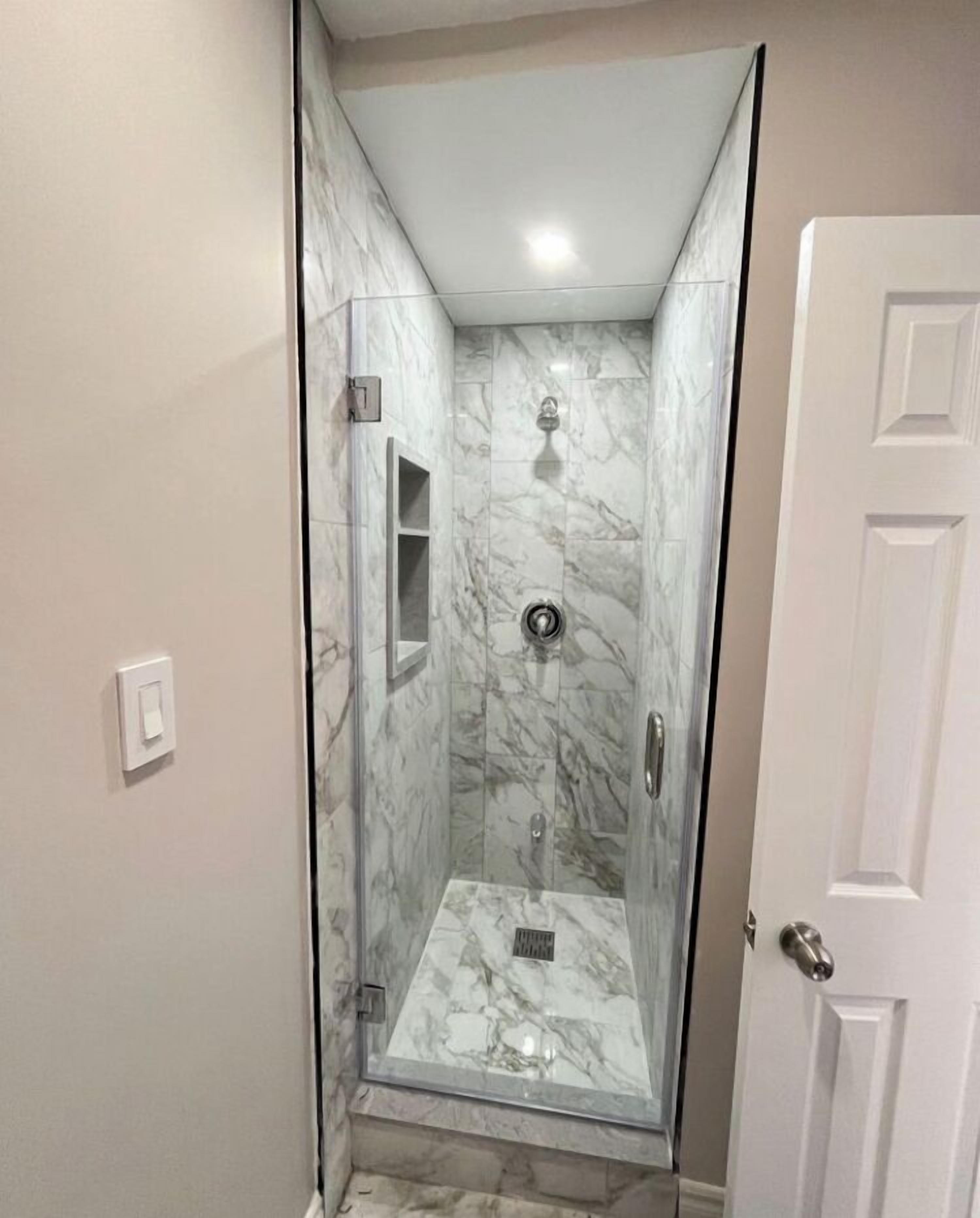 A walk-in shower with marble walls and a glass door.