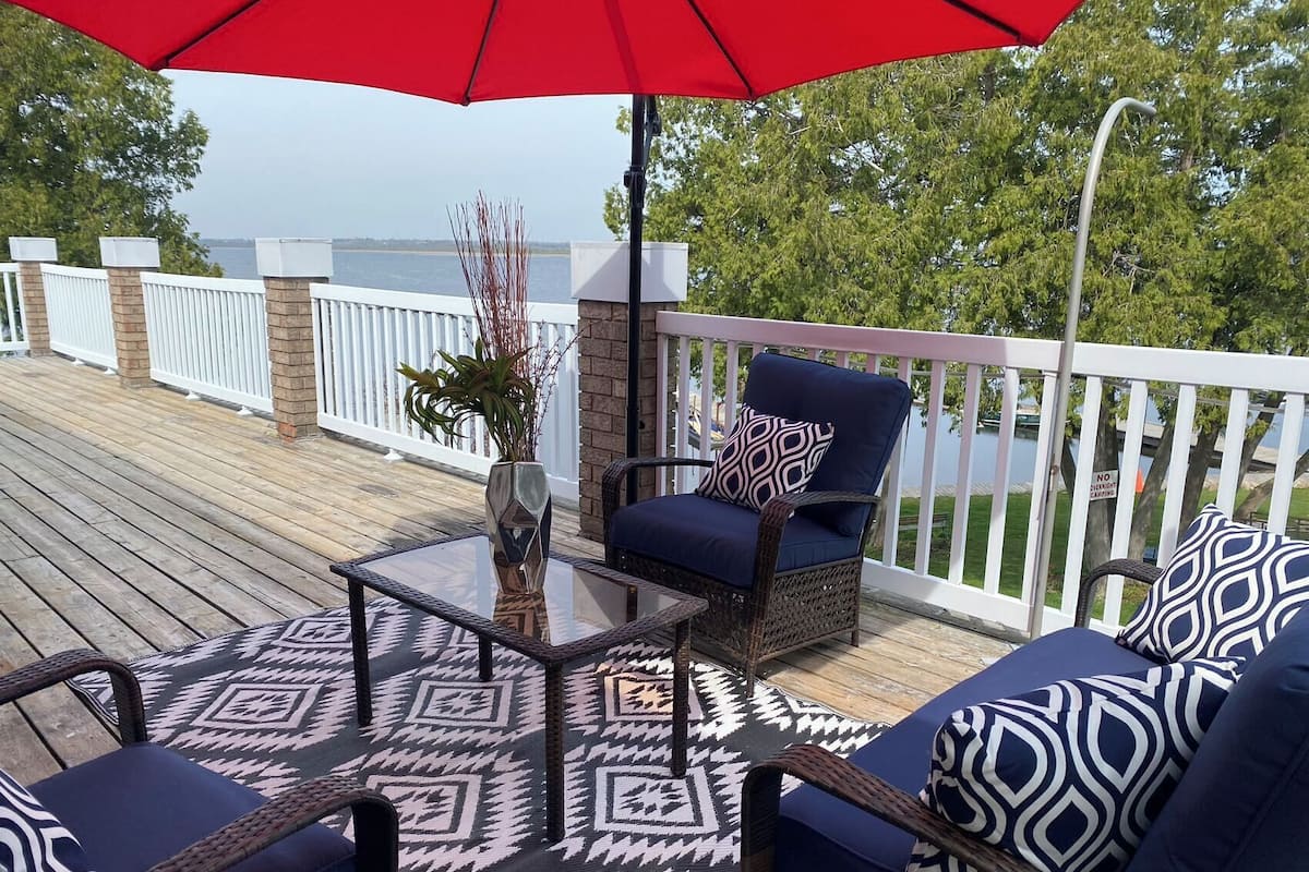 A deck with wicker furniture, a glass table, and a red umbrella.