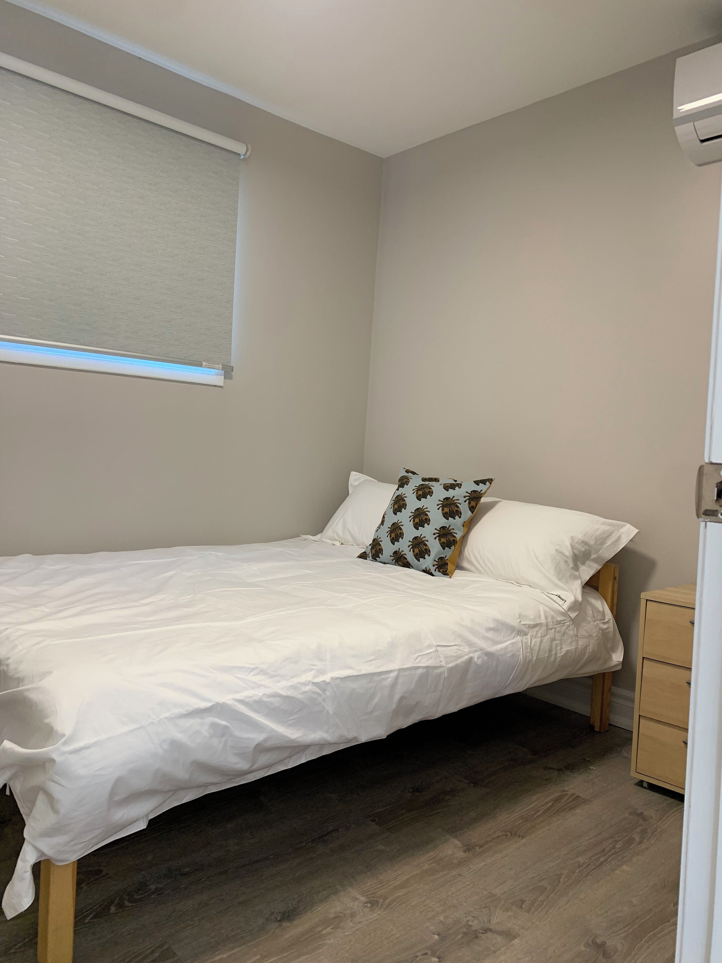 A small, neatly made bed with white bedding and two pillows, one with a palm leaf pattern.