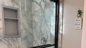 A bathroom with a glass-enclosed shower, a toilet, and a small shelf.