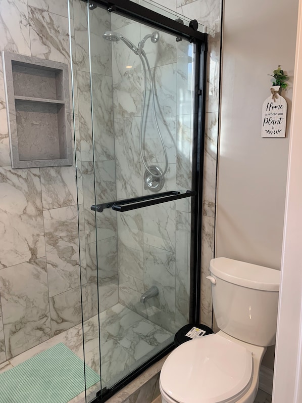 Un baño con ducha de vidrio, inodoro y una pequeña estantería.