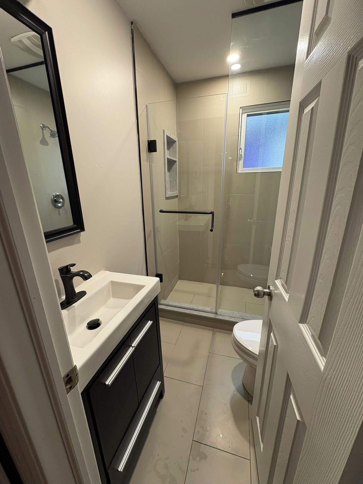 A modern bathroom with a glass shower enclosure, a white sink, and a toilet.