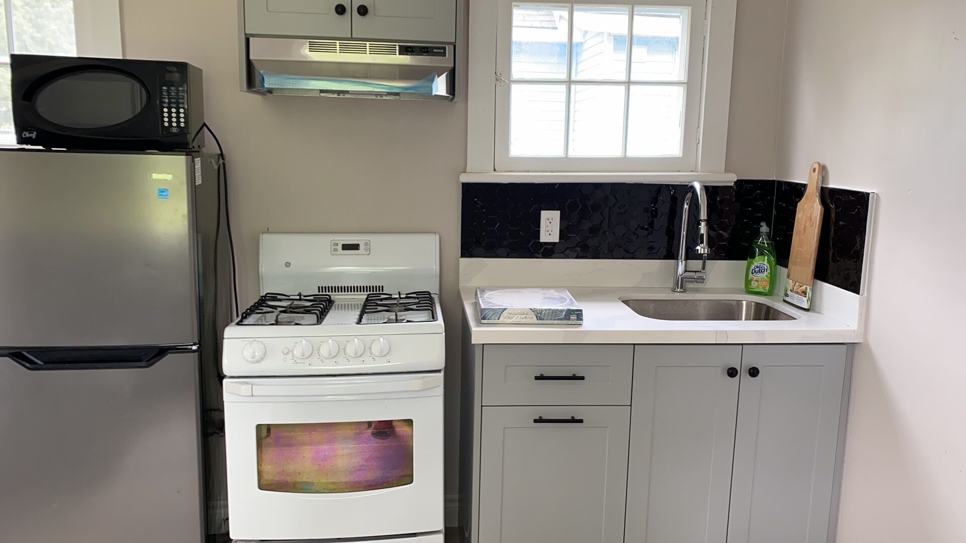 A compact kitchen with a refrigerator, stove, microwave, and a window above the sink.