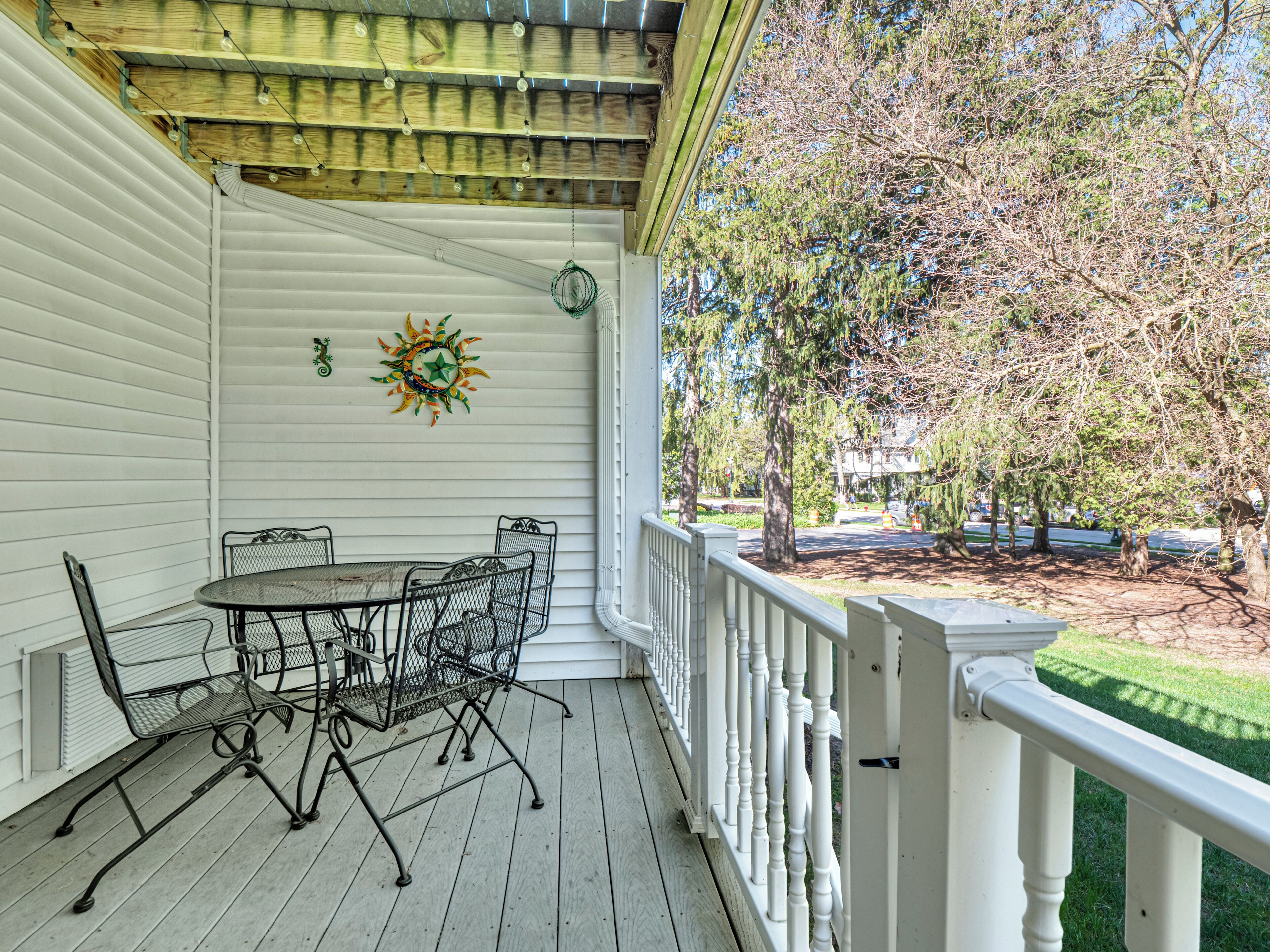 A covered porch with a table and chairs, a decorative sun, and a view of trees and a street.