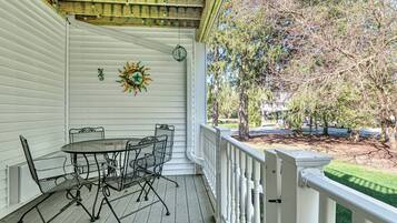 A covered porch with a table and chairs, a decorative sun, and a view of trees and a street.