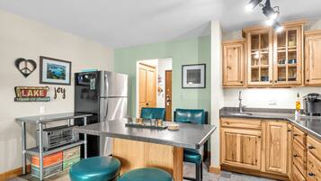A kitchen with a stainless steel refrigerator, wooden cabinets, a granite countertop, and teal bar stools.