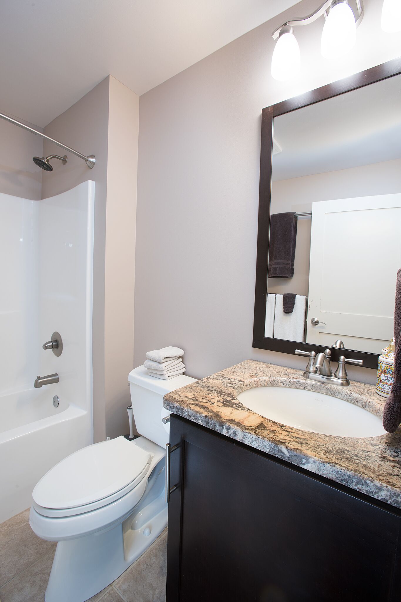 A modern bathroom with a white toilet, a sink with a granite countertop, a large mirror, and a shower area.