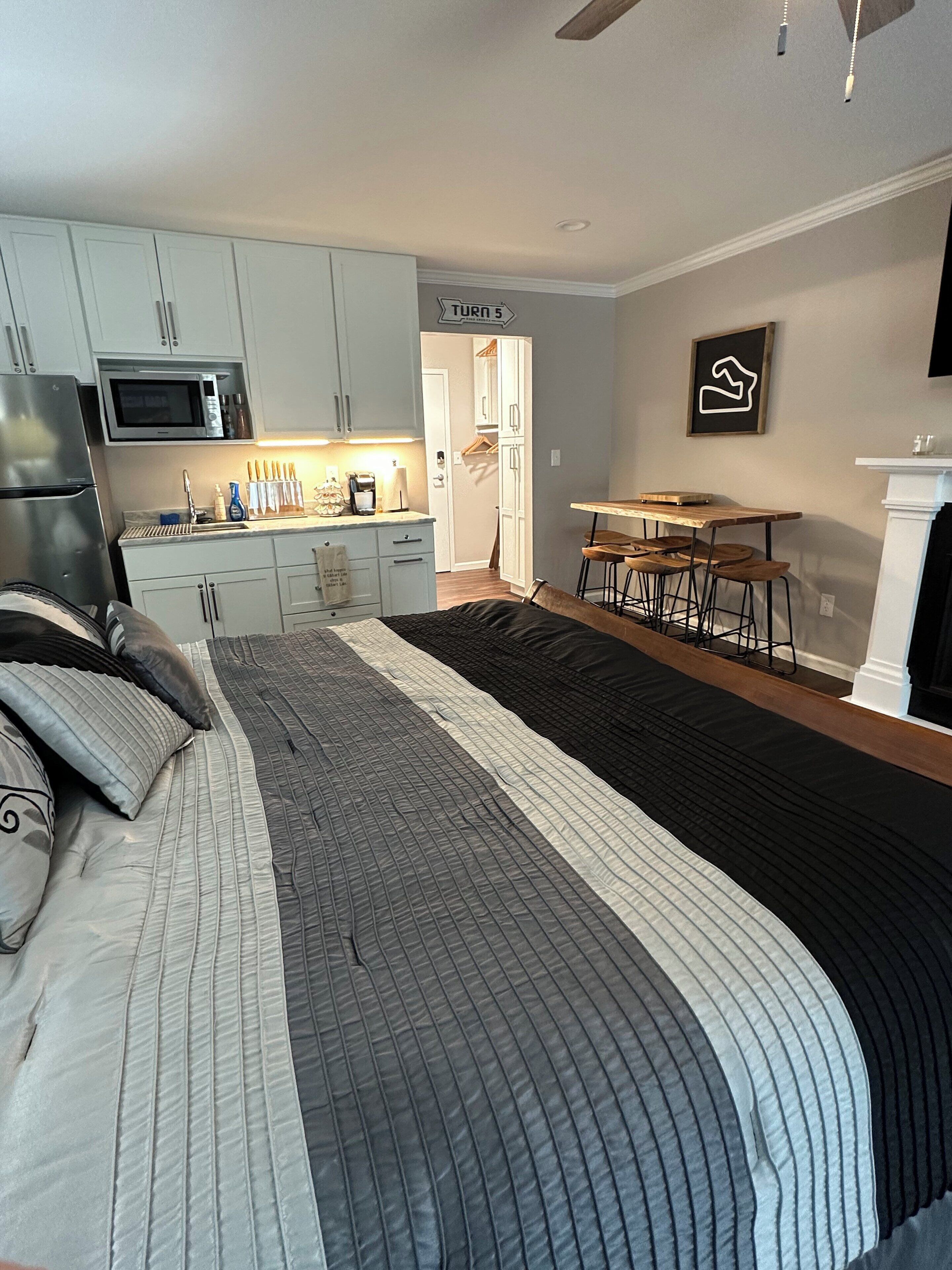 A bedroom with a bed, a kitchenette, a dining area, and a hallway leading to another room.