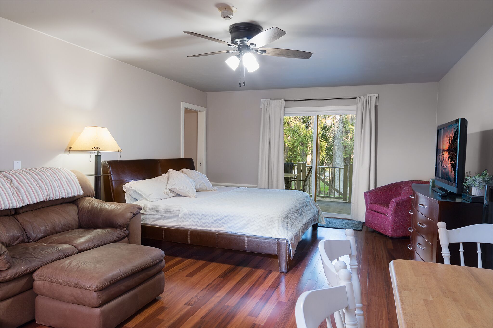 A bedroom with a bed, a ceiling fan, a window with curtains, a TV, and a sofa.