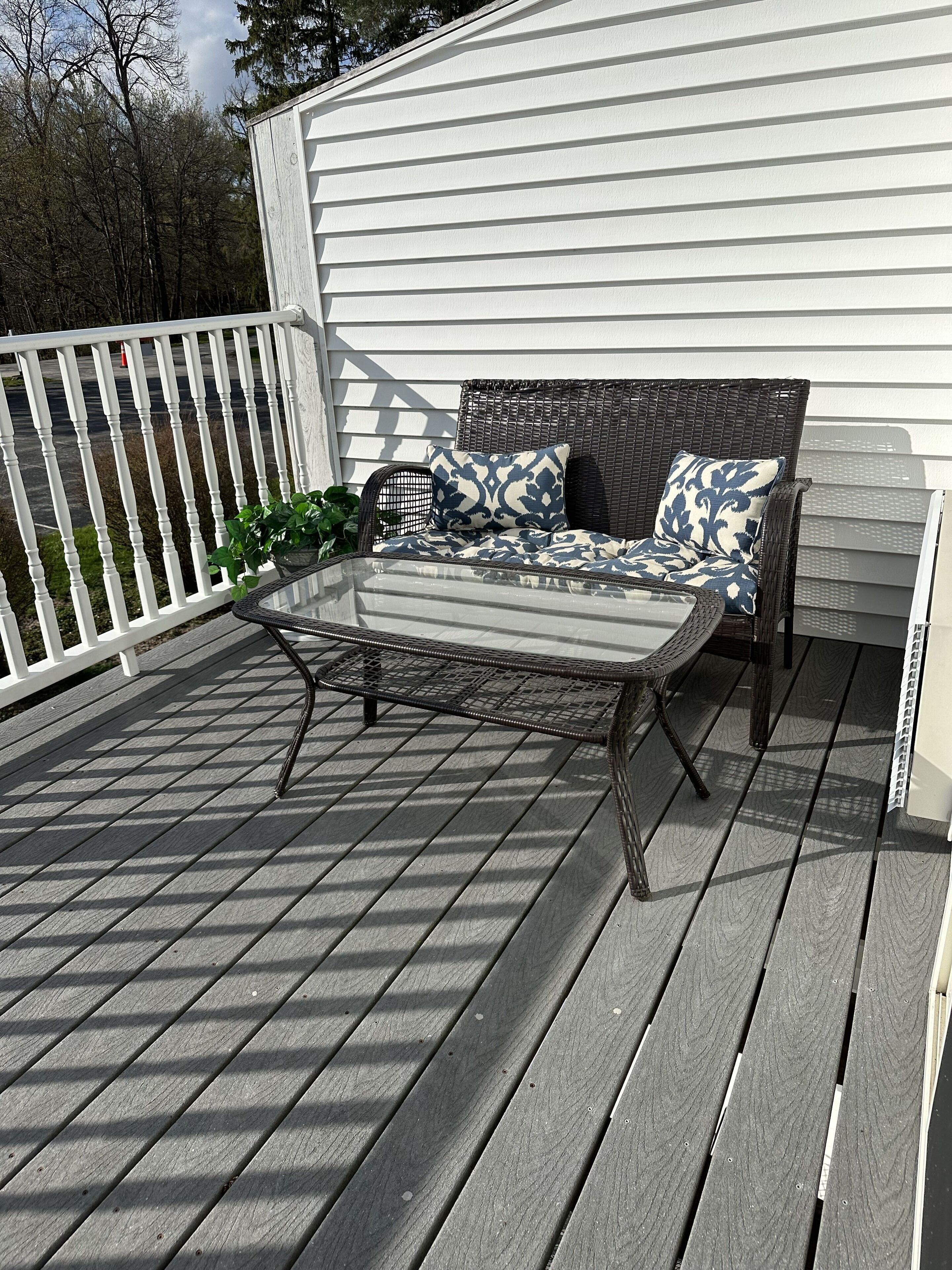 Une terrasse dotée d’une table en métal et de mobilier en osier, entourée d’une rambarde blanche et d’une plateforme en bois.