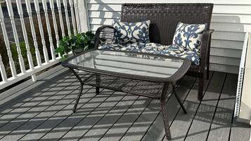 Une terrasse dotée d’une table en métal et de mobilier en osier, entourée d’une rambarde blanche et d’une plateforme en bois.