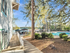 A wooden deck leading to a pool area with a fenced swimming pool, surrounded by trees and a building with a balcony. - Victorian Inn Elkhart Lake Wisconsin (Elkhart Lake)
