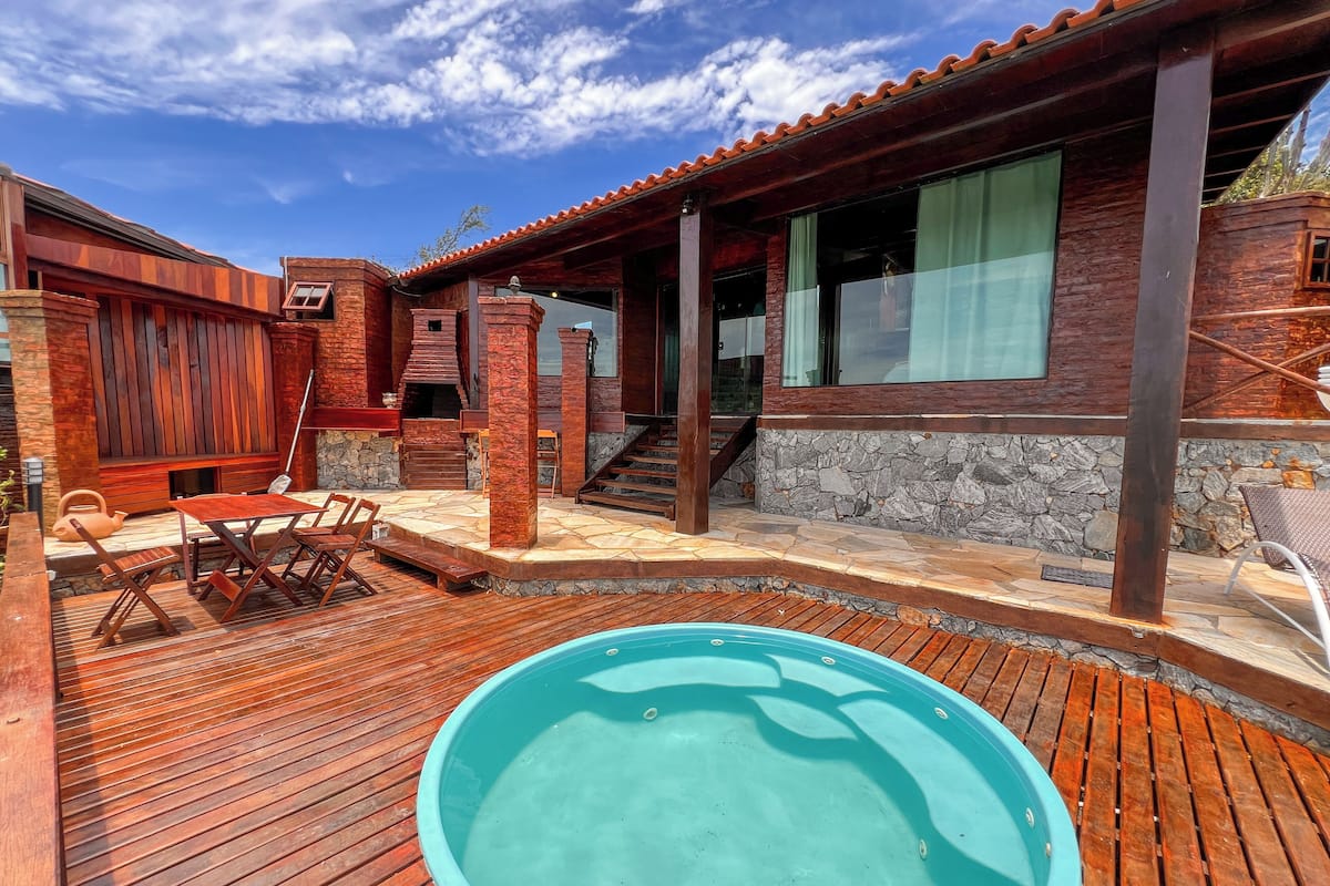 Una terrazza in legno con piscina, pareti in pietra e un'area patio coperta.
