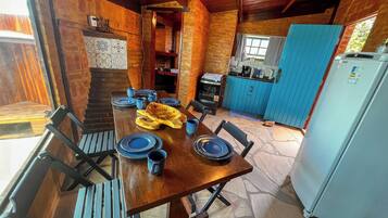 Uma área de jantar rústica com uma mesa de madeira posta para quatro pessoas, cercada por paredes de pedra e um armário azul.