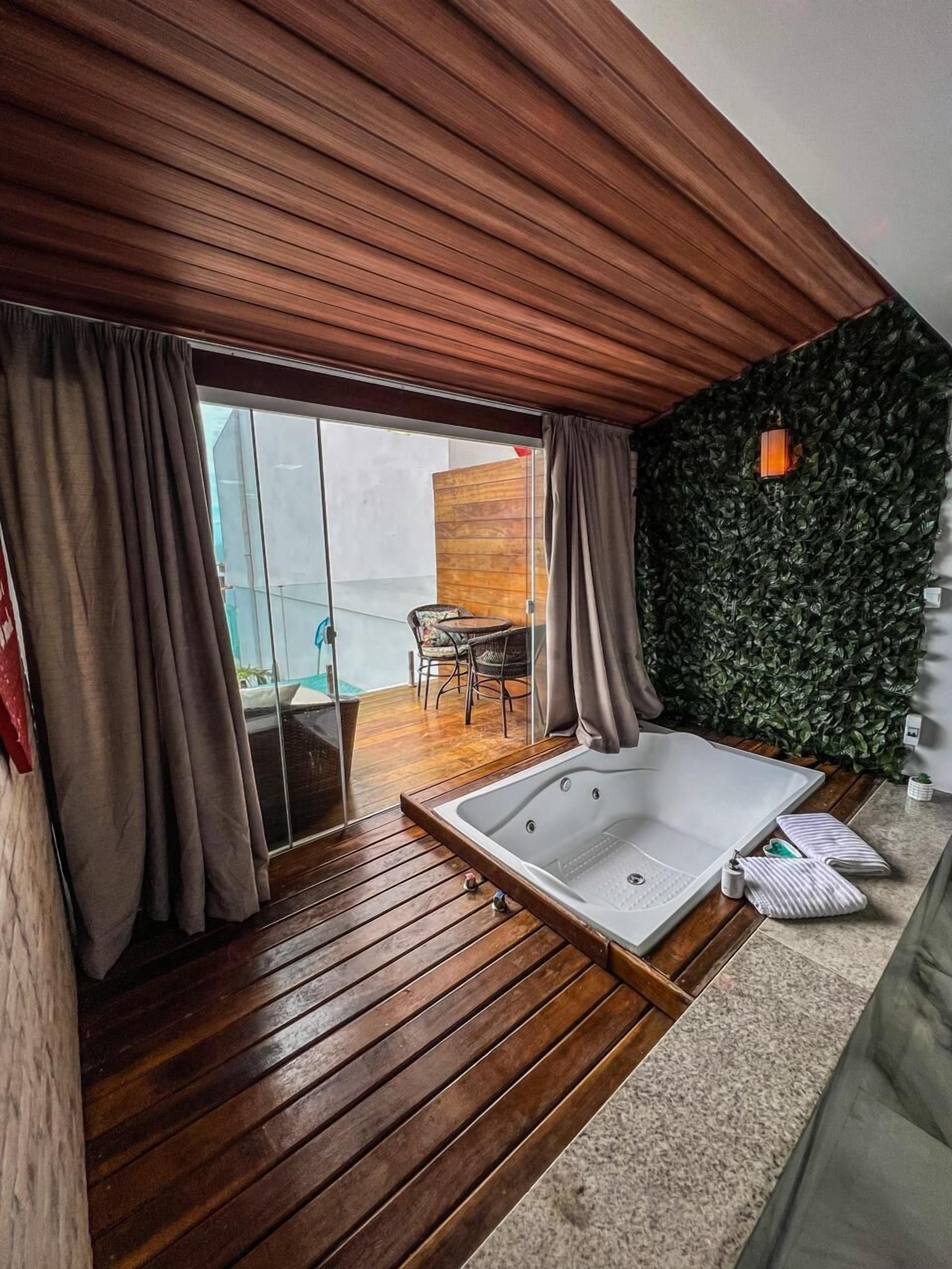 Une salle de bain moderne avec un plancher en bois, une grande baignoire et une porte coulissante en verre donnant sur un balcon équipé d’une chaise et d’une table.